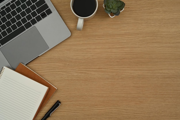 Top view simple workplace with laptop potted plant coffee cup and notebooks on wooden table