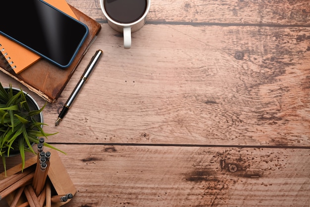 Photo top view of simple workspace with smartphone, coffee cup, notebook and houseplant on wooden desk.