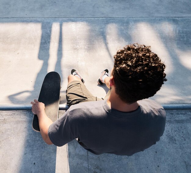 Vista dall'alto dell'uomo skater e dello skateboard in strada cittadina o all'aperto sport di skateboard e uomo seduto sulla rampa che si prepara per l'esercizio di pattinaggio o allenamento fitness e allenamento in città