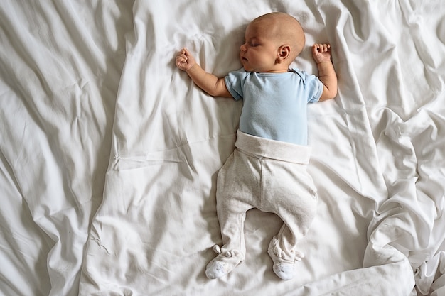 Top view of sleeping baby lying on bed with white sheet, copy space