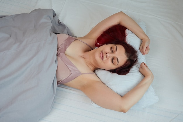 Top view sleeping beautiful woman waking up in her bed stretching smiling.