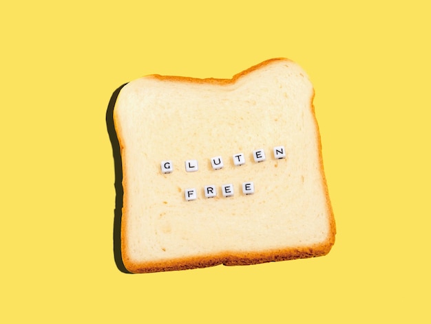 Top view slice of bread and word cubes with inscription gluten free Gluten free bread concept on yellow background