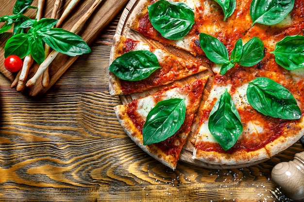 Top view on sliced margarita pizza with ingridients on wooden background. Mozzarella, basil, cherry tomato. Copy space for design. Picture for menu, italian cuisine