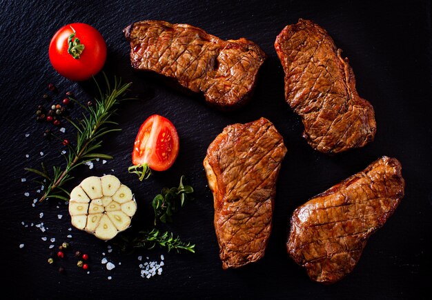 Top view of slices of a grilled steak with tomatoes garlic and spices on a dark background