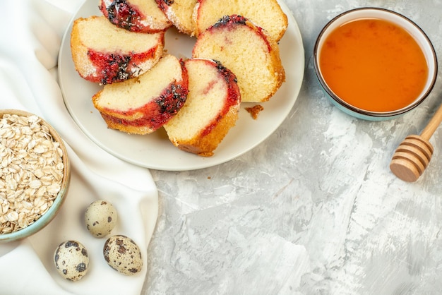 Top view slices of jam cake on plate honey and oats in bowls quail eggs on table