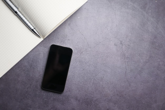 Top view of smart phone with empty screen and notepad on gray background