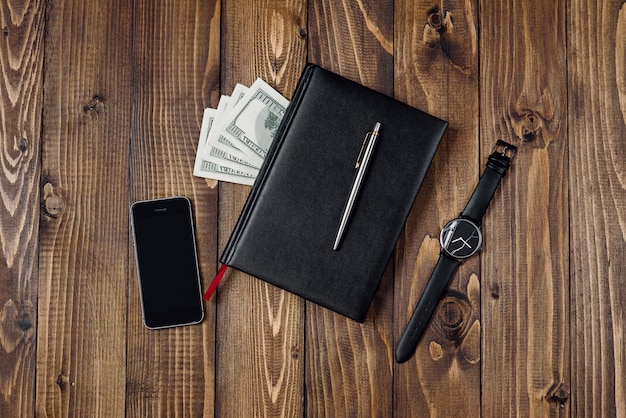 Top view of smartphone, watch, pen, notebook and money