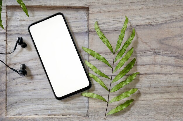 Top view smartphone with blank screen and earphone on wooden background.