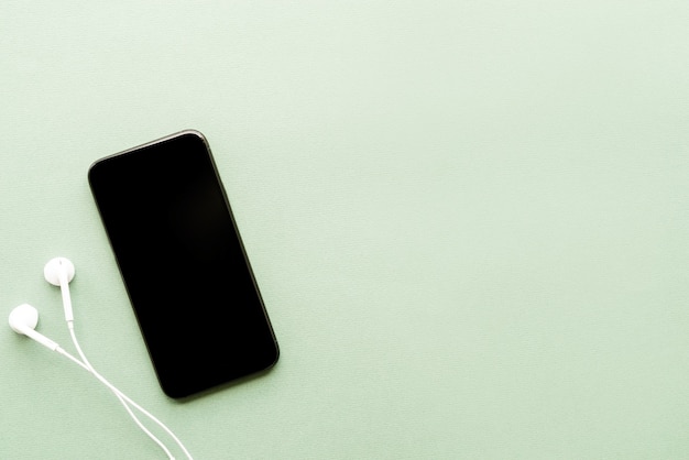 Photo top view of smartphone with blank screen headphones on green background