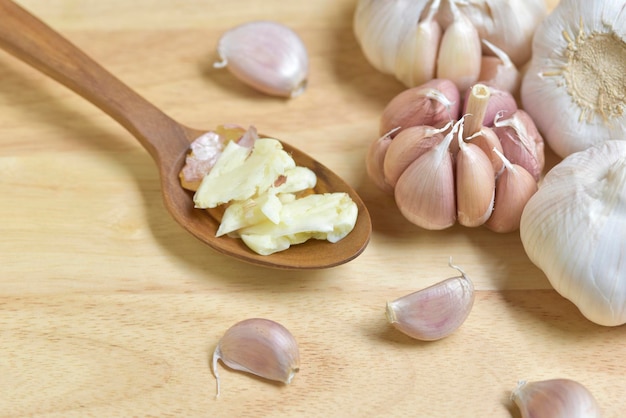 Photo top view smashed garlic in a wooden spoon along with garlic bulbs and garlic cloves on wood background concept of spices for healthy cooking selected focus