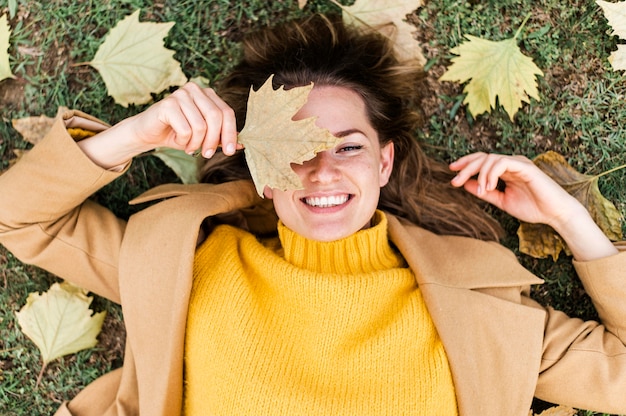 Top view smiley young woman staying on the ground next to autumn leaves