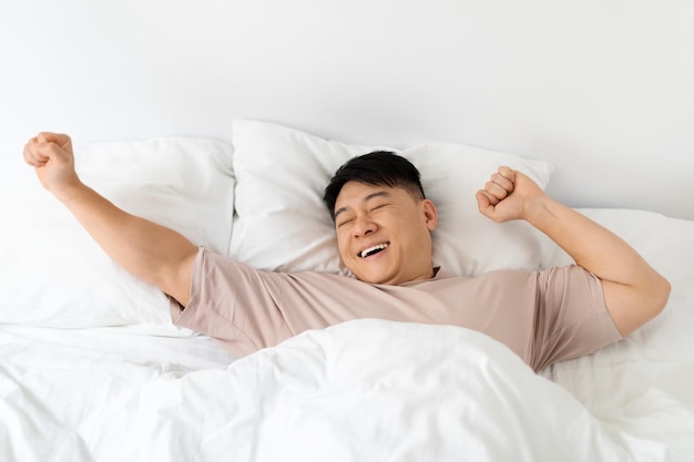 Top view of smiling asian man stretching in bed