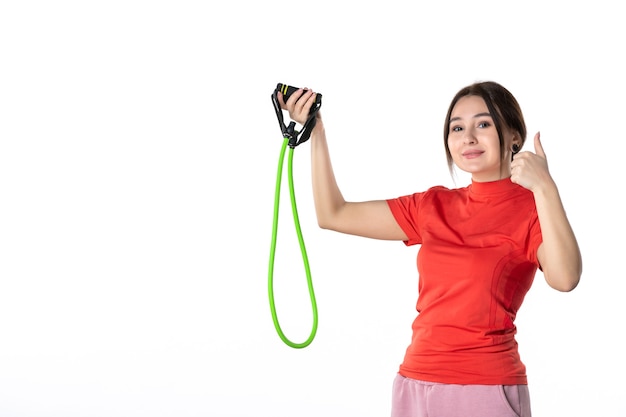 Top view of a smiling confident young woman neatly gathering her hair dressed in redorange blouse and holding rope sport accessory making ok gesture on white background