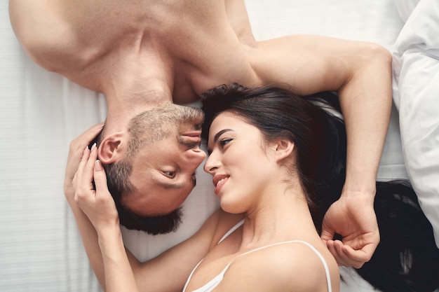 Photo top view of a smiling lovely young woman and a handsome man daydreaming in bed