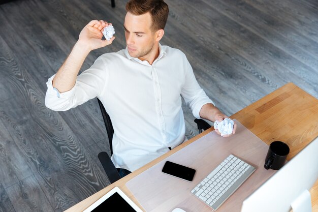 Top view of smiling relaxed young businessman sitting and using smartphone in office