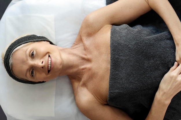 Photo top view of smiling senior woman laying at the couch after making an effective facial procedure