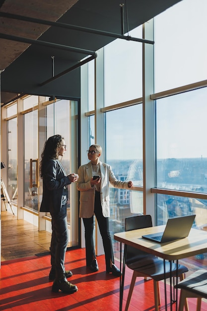 Top view of smiling young confident business workers in casual clothes standing on modern office background and talking during day break