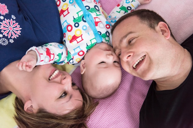 Top view of smiling young couple lying together with their adorable baby boy on blankets in their living room at home