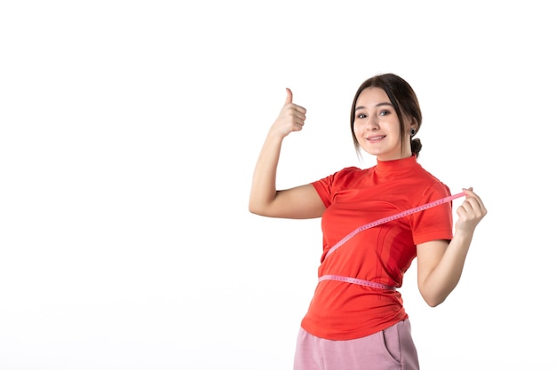 Top view of a smiling young lady gathering her hair dressed in redorange blouse and holding metre measuring her waist making ok gesture on white background