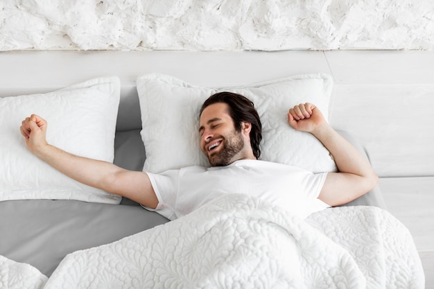 Top view of smiling young man stretching in bed