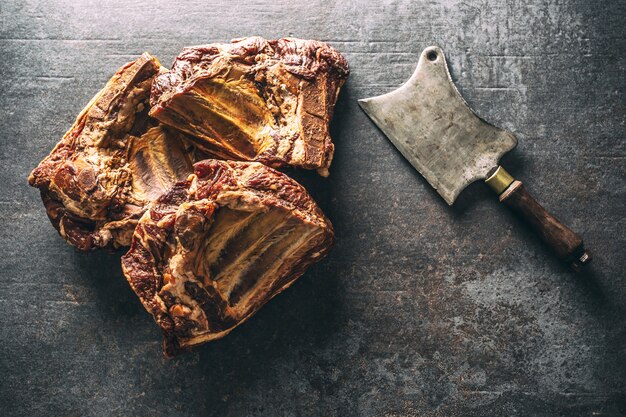 Top view of smoked ribs on a dark metallic surface next to a vintage knife.