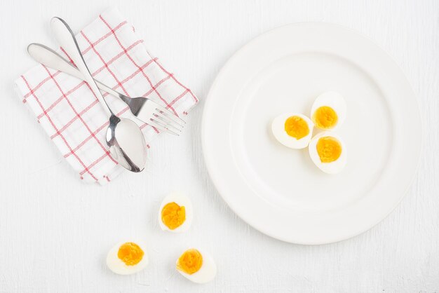 白い木製のテーブルの上に置かれた白いプレート上のソフトボイルド卵とスプーンの上面図