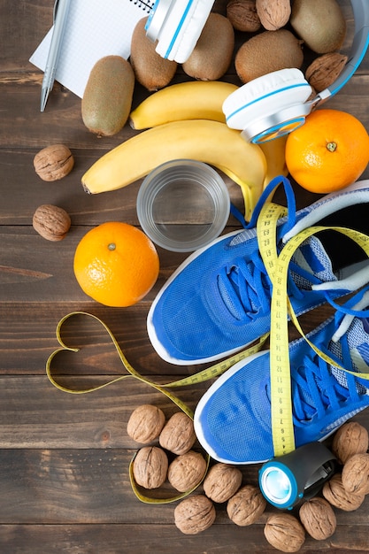 Foto vista dall'alto di alcuni cibi naturali, scarpe da ginnastica e metro a nastro su un tavolo di legno scuro. concetto di salute, cibo e sport.