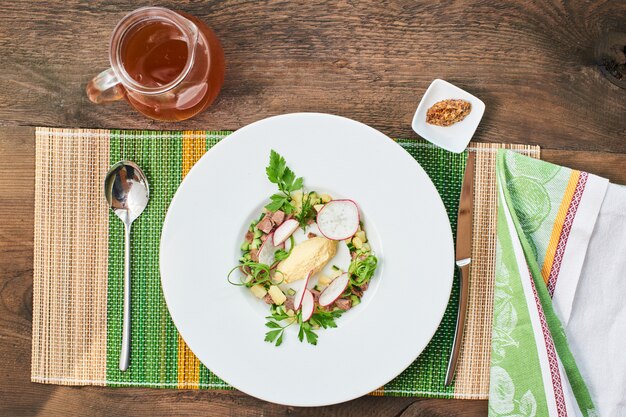 Top view of the soup with beef in a white plate and a pitcher of brew on a wooden table