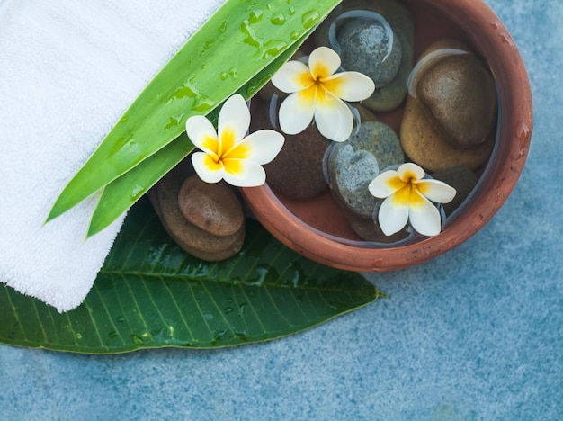 Top view of spa objects stones green leaves and flowers for massage treatment on blue background
