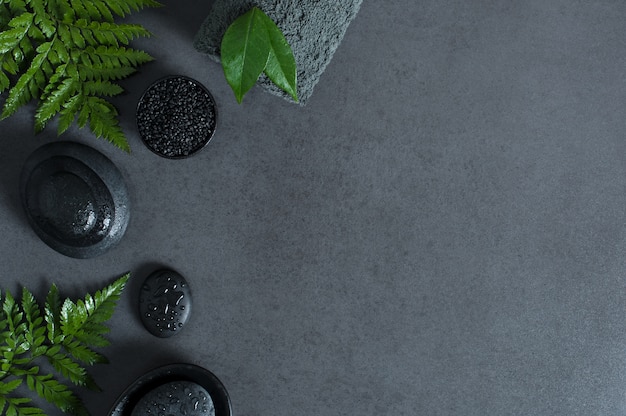 Photo top view of spa setting with hot stones and green ferns on gray background with copy sapce.