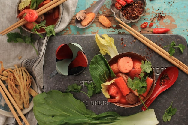 사진 녹색 나무 배경에 소박한 갈색 그릇에 제공되는 해산물을 곁들인 매운 태국식 톰 얌 수프 상위 뷰