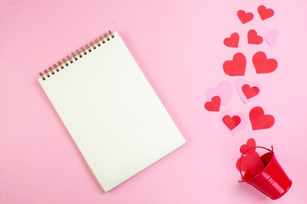 top view spiral notebook red heart stickers scattered from bucket on pink background