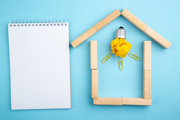Фото Вид сверху спиральный блокнот мятой бумаги с идеей концепции лампочки в деревянных блоках в форме дома на синем фоне