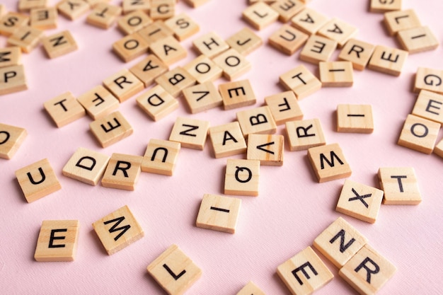 Top view of square wooden tiles with the English alphabet lying on a pink background