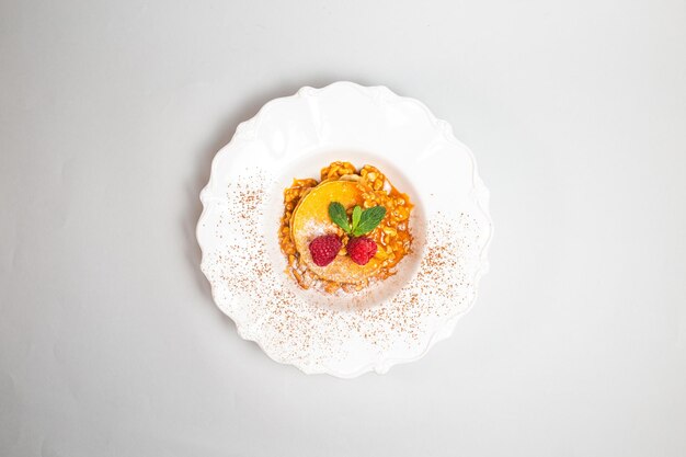 Top view of a stack of pancakes with raspberries and mint on white plate