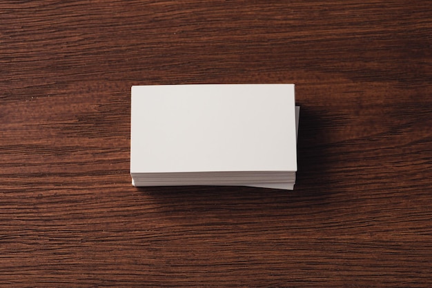 Top view of stacked white business cards on brown wooden surface