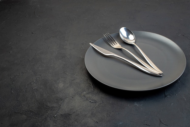 Top view of stainless cutlery set on a black plate on the left side on dark color background with free space