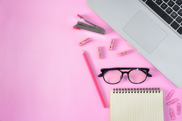 Top view of stationery or school supplies with books, color pencils, laptop, clips and glasses on pink background with copyspace. Education or Back to school concept.