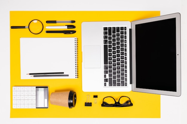 top view of stationery with laptop, notepads, magnifier and calculator on yellow surface