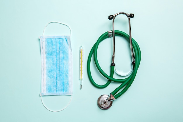 Top view of stethoscope, mercury thermometer and a protective face mask