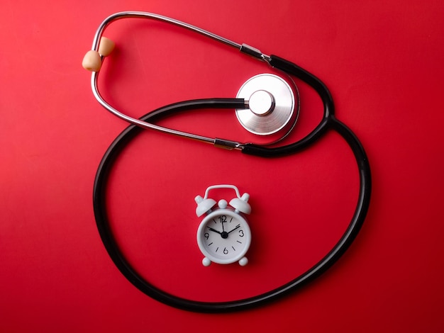 Photo top view stethoscope and white alarm clock on a red background