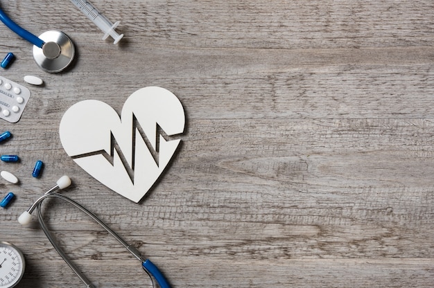 Top view of stethoscope with heart having cardio sign and medicine on doctor desk.