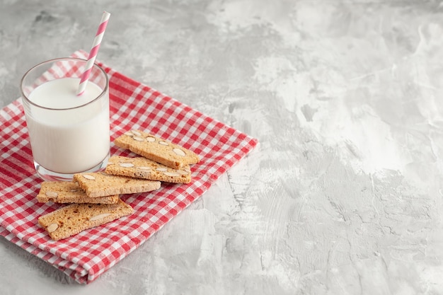 Top view of stick shaped candy in glass cup and pastries on red stripped towel on the right side on gray background