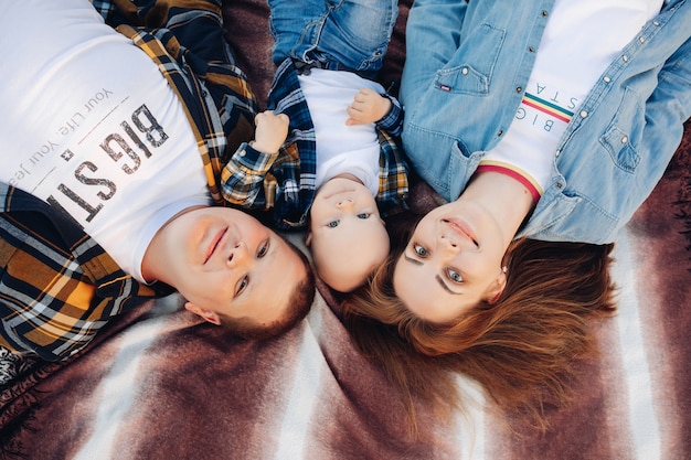 Top view stock photo of happy young family of mother, father and toddler son smiling at camera laying on bed.