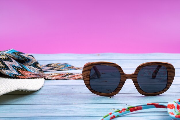 Top view of a straw white hat with glasses and a swimsuit lying on a blue wooden backgroundsummer vacation concept