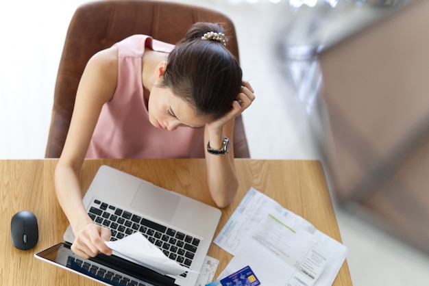 Top View Of Stressed Young Sitting Asian Woman Hand Holding The Head Worry About How To Find Money To Pay Credit Card Debt And All Loan Bills.