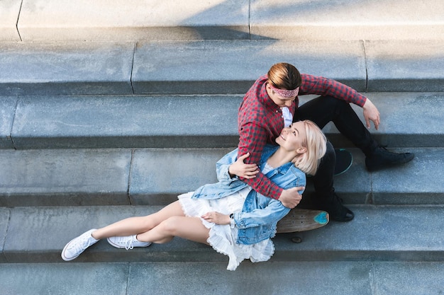 Вид сверху стильной пары подростков с лонгбордом сидит на бетонной лестнице