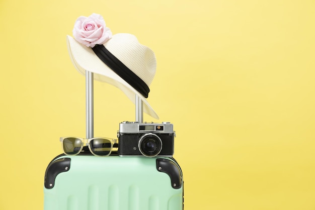 Top view of a suitcase, sunglasses, camera and hat on a yellow background - vacation concept