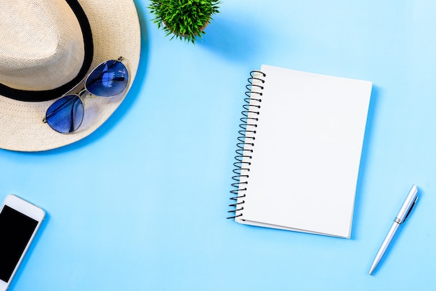 Top view summer travel planning concept with white hat, blue eyeglasses, phone and notebook