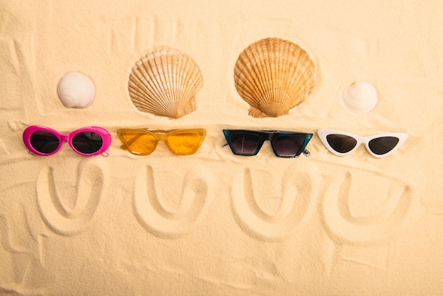 Top view of sunglasses and seashells with smiles drawn on sand